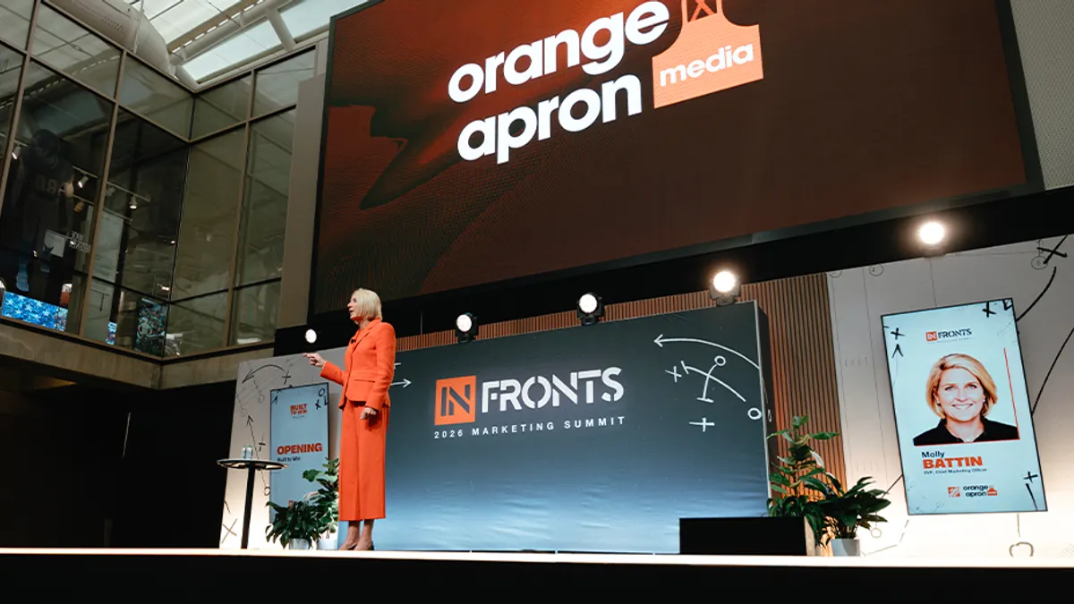 An executive wearing an orange suit presents on stage in front of a wall reading InFronts