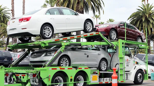 A Jack Cooper Transport truck delivers a load of new Chevrolets and Buicks to a dealership in the sun in Newport Beach, California, in 2018.