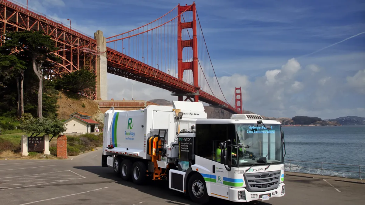 A waste collection truck with Recology branding sits in a parking lot with the Golden Gate Bridge in the background.