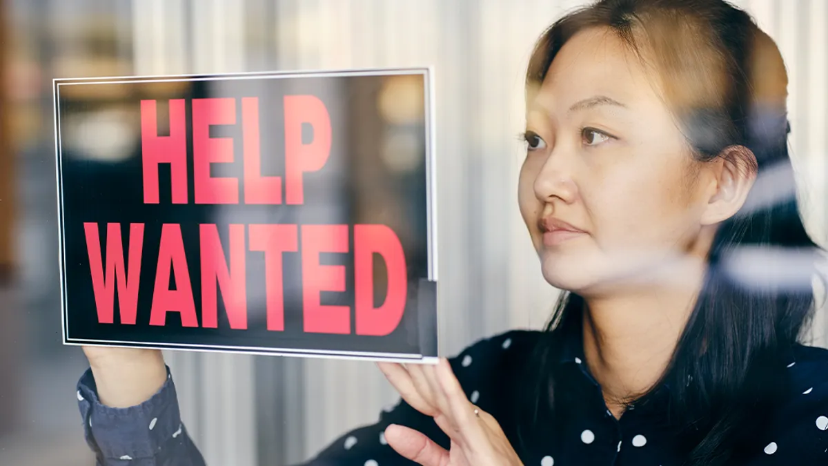 Business owner putting up help wanted sign in a window.