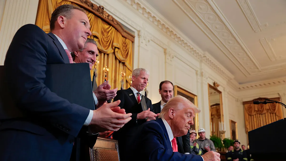 Lee Zeldin claps next to Donald Trump as he signs an executive order, amid a crowd of people