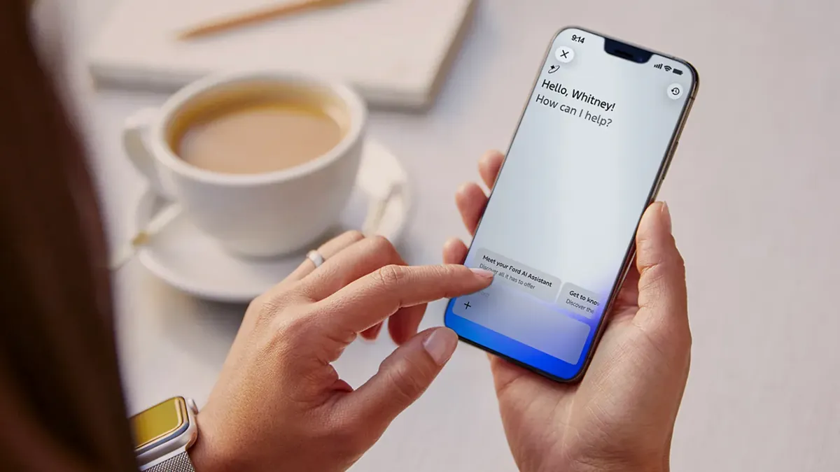 A person using the Ford vehicle app on a smartphone with a cup of coffee shown on a table.