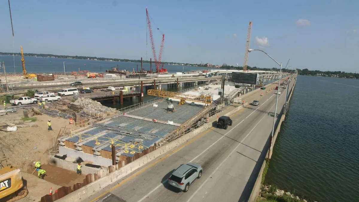 Aerial view of multiple concrete bridge structures stretching across water, with cranes and other construction equipment working on the jobsite.