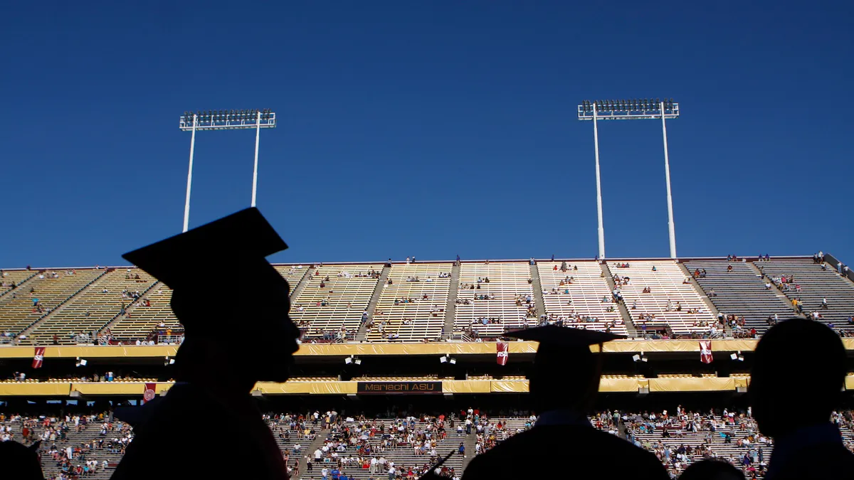 Silhouettes of Arizona State University students are in front of a background of bleachers at a graduation ceremony.