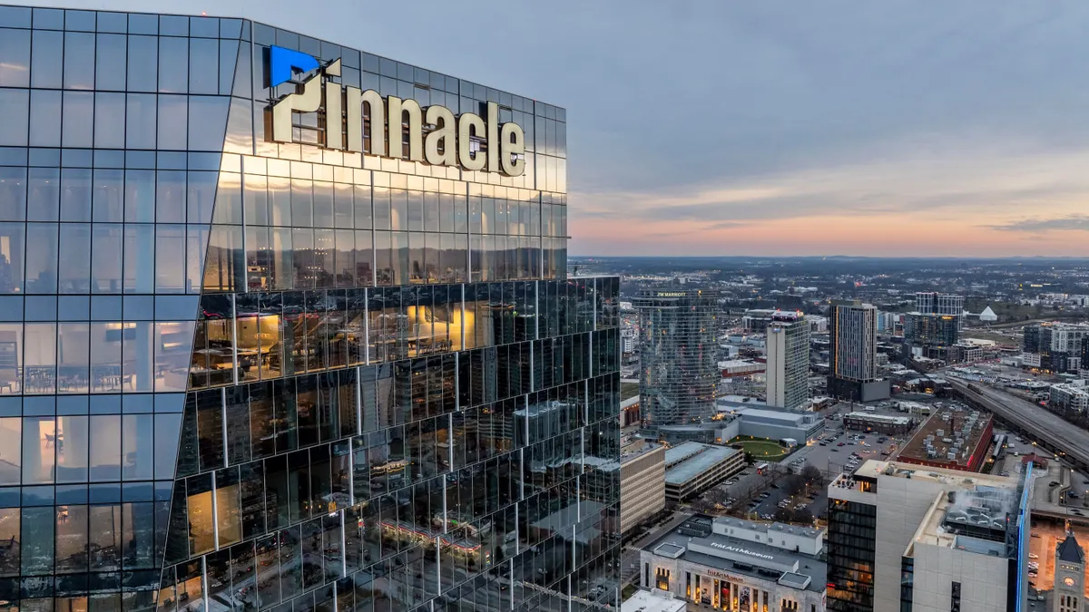 A glass office building with the word "Pinnacle" and its logo on the exterior is seen from high above Nashville's downtown.