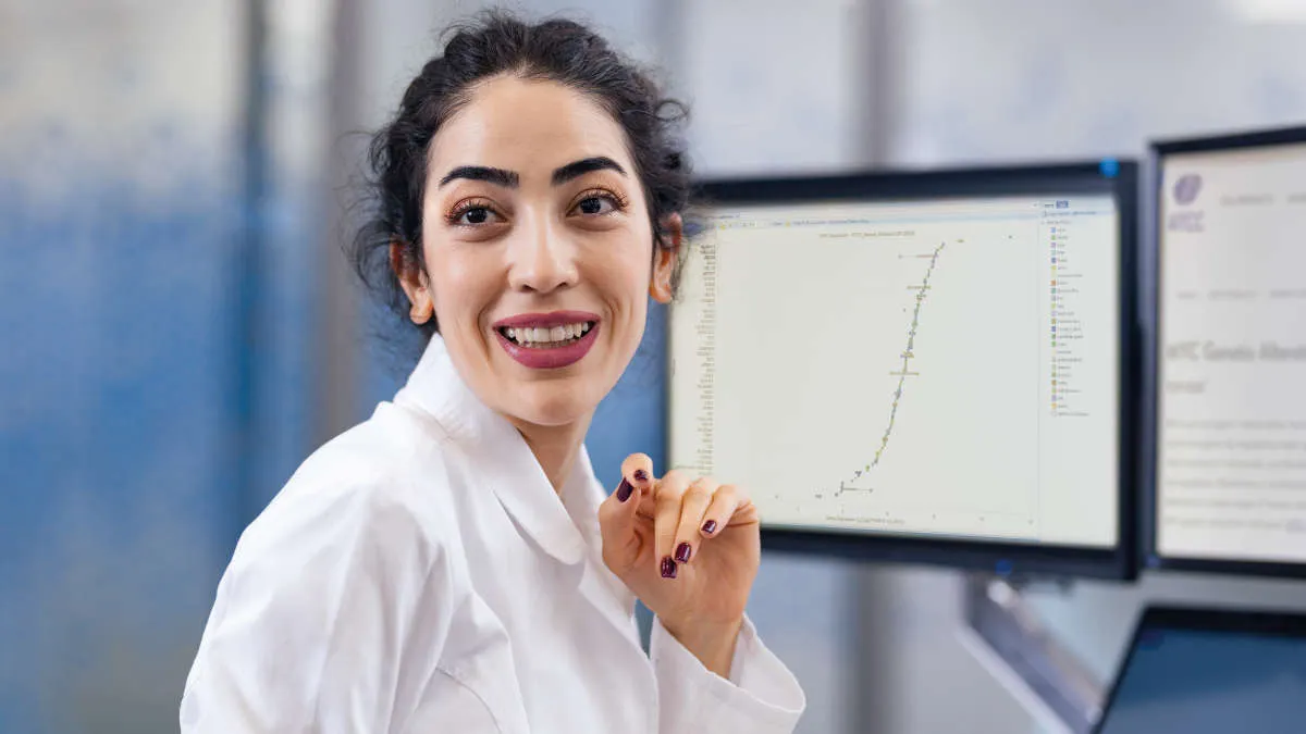 Woman in white coat looking at data ang line charts on monitors