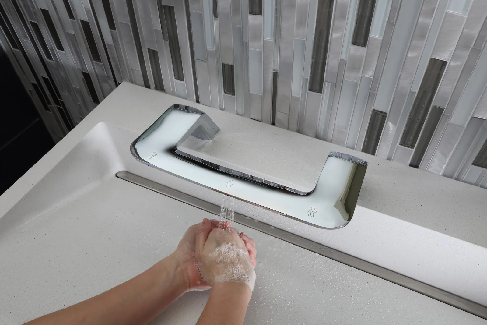 A photo of a three-in-one bathroom fixture. The ficsture is silver, the basin is white and the wall is black and white. A person is washing their hands.