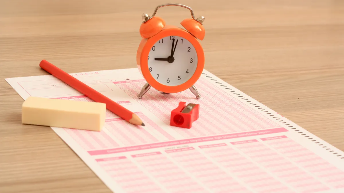 A clock stands on top of a multiple choice testing sheet near a pencil, eraser and pencil sharpener.