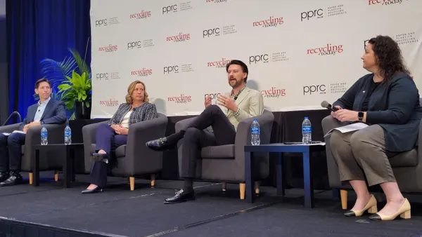 Four people sit in chairs on a stage in front of a background that says Paper and Plastics Recycling Conference, while one person speaks.