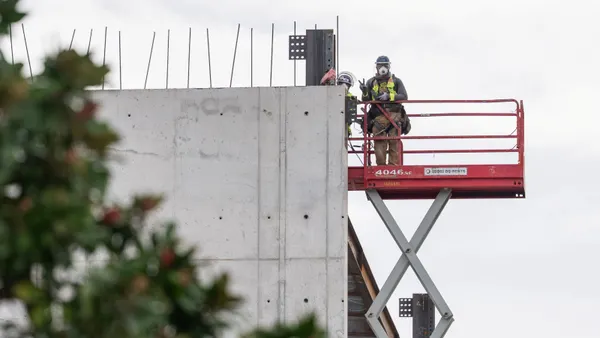A construction worker on a lift flashes the peace sign toward the camera.