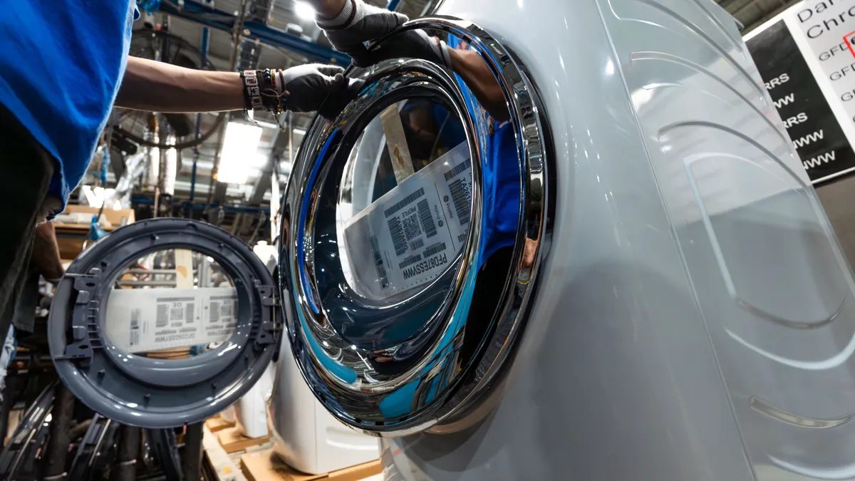 A worker attaches a component onto a laundry machine.