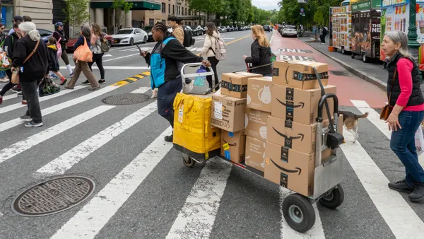 A person pulls a trolley with Amazon packages across the street at a crossing.