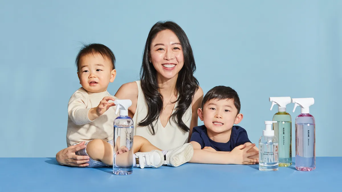 Person smiling wiht brown hair next to two young children and cleaning bottles