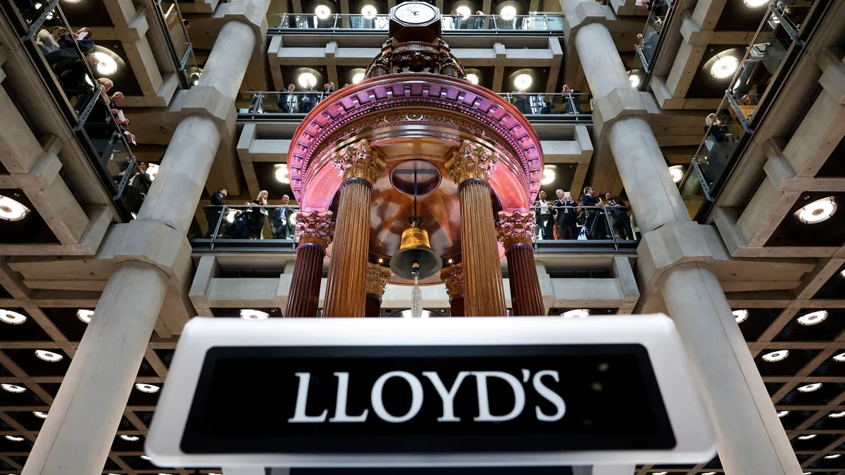 A large bell on a pedestal that depicts the Lloyd's logo is seen in a multistory atrium.