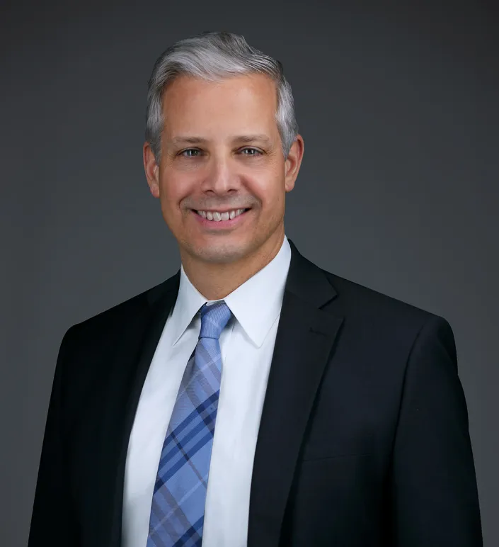 A person in a dark suit, white shirt and patterned tie