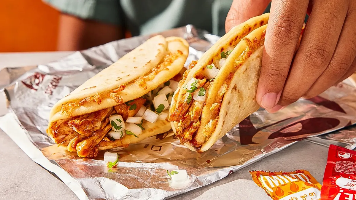 A picture of a hand lifting a Chicken Al Pastor Street Chalupa with another in the background.