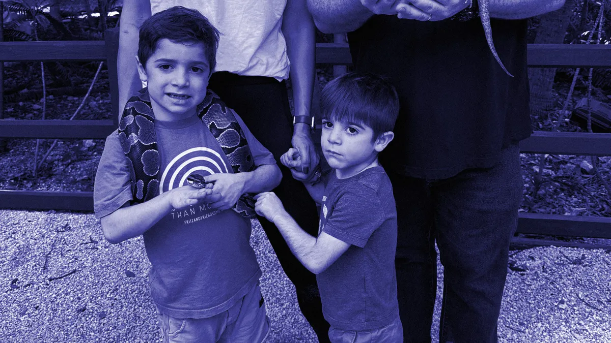 Two young boys are seen posing for a photograph with a snake.
