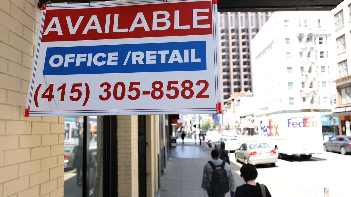 A sign outside of a city building reads "Available" and "office/retail" as people walk by on the sidewalk