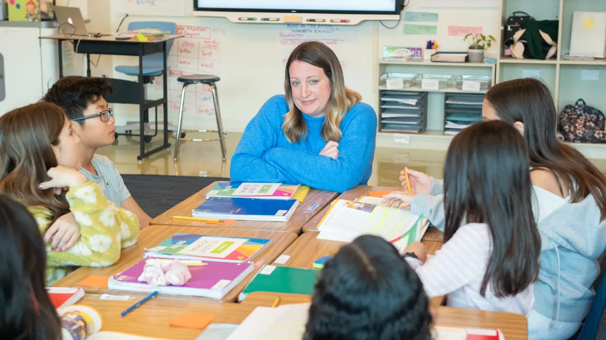 A teacher at the end of a desk group with kids working in their school workbooks