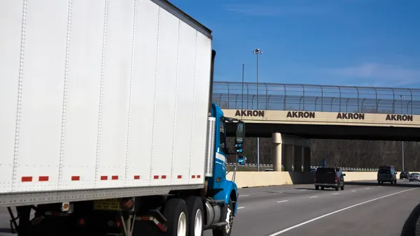 A tractor-trailer travels on the road headed toward an underpass with the words Akron listed on the overpass.
