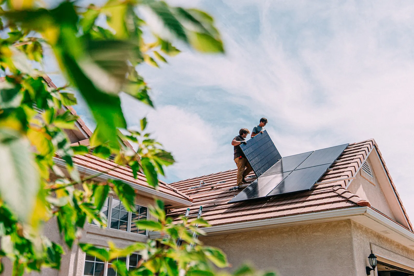 Two people install a solar panel on the roof of a house.