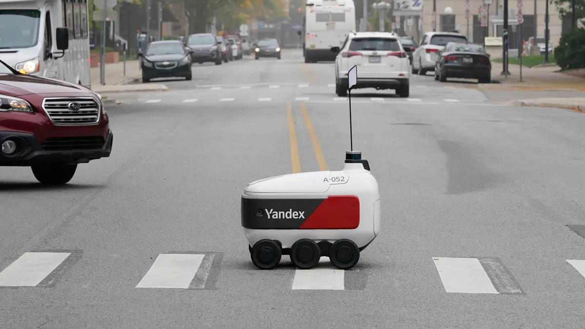 A delivery robot crosses a busy street.