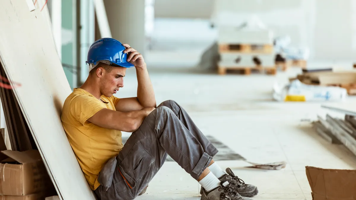 A construction worker sits on the jobsite, leaning on a piece of material.