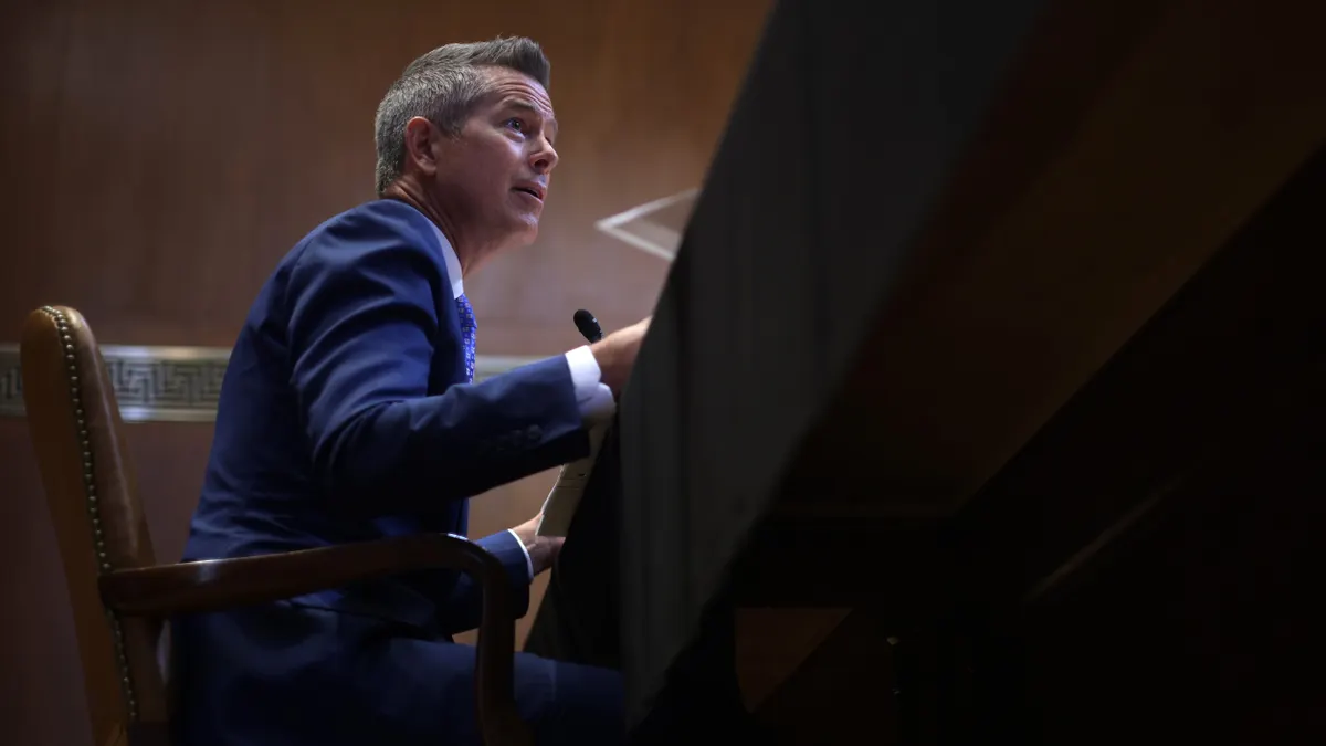 A person in a blue suit in a chair at a desk seen from a low angle.