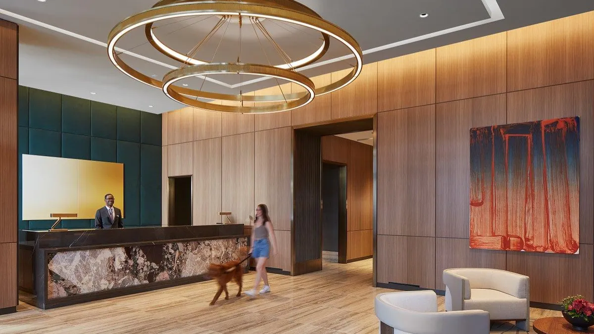 A lobby area with white chairs. Someone is behind the front desk and another person is walking a dog.