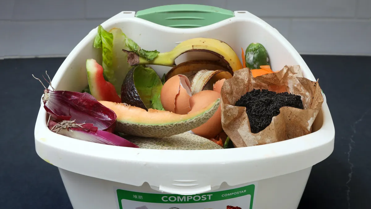 A small white plastic pail with food scraps and a label on composting guidelines