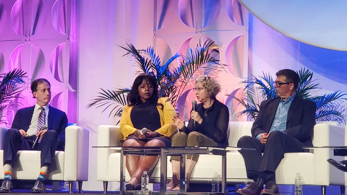 Four people sit on a stage, and one of them speaks into a microphone.