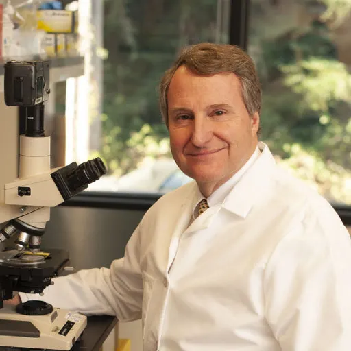 Steven Quay seated beside a microscope in a laboratory.