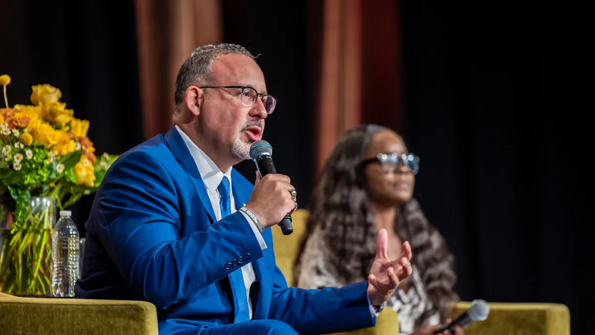 U.S. Department of Education Secretary Miguel Cardona speaks into a microphone while making a hand gesture