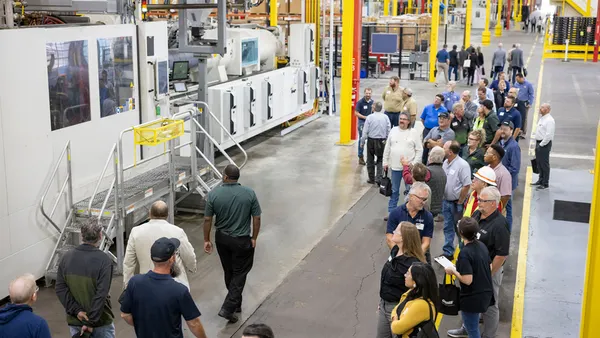 Dozens of people viewing heavy equipment in an industrial facility.