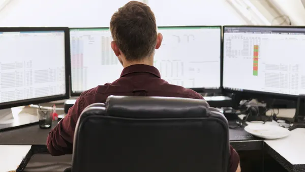 Rear view of a young businessman working on a computer with multiple monitors in a modern office.