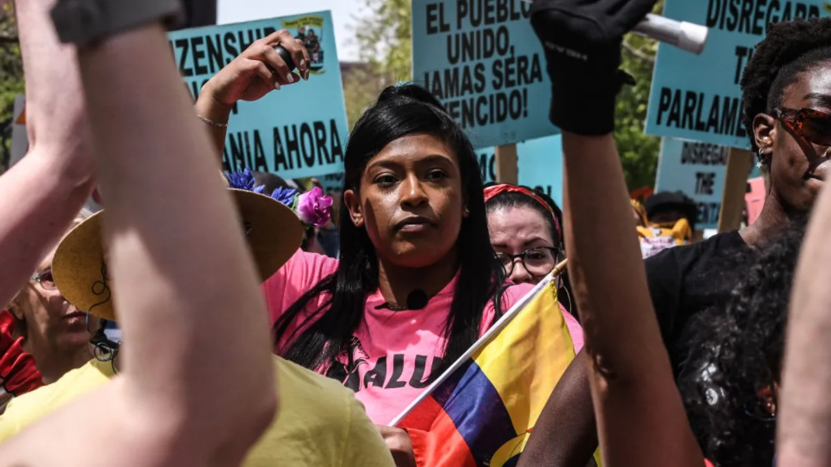 A medium-skinned person joins a protest, with pro-union signs in Spanish behind them