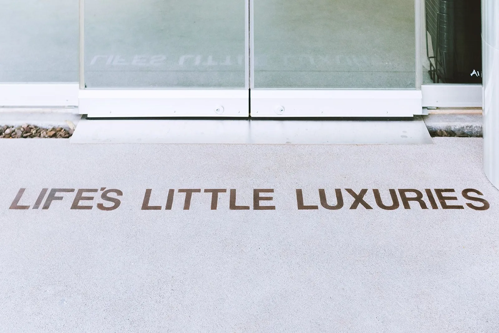 A photo of words in the concrete outside of Air Guitar in Gilbert, Arizona, saying Life's Little Luxuries.