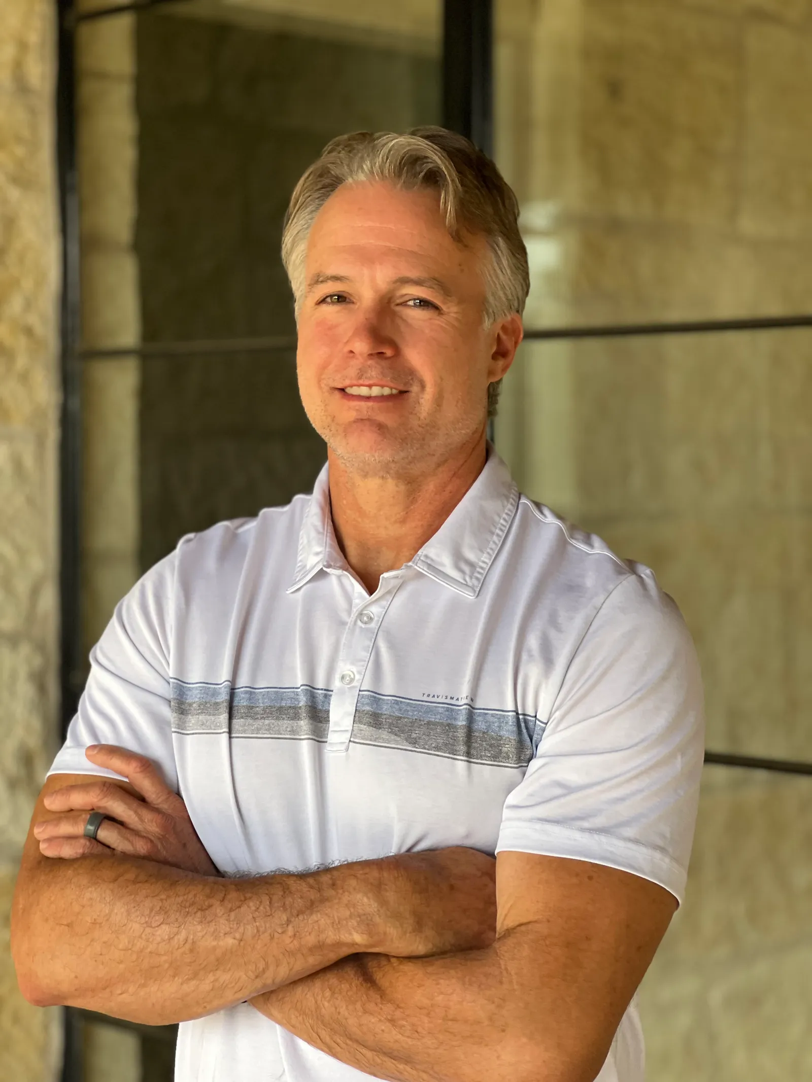 A man wearing a polo stands with his arms crossed