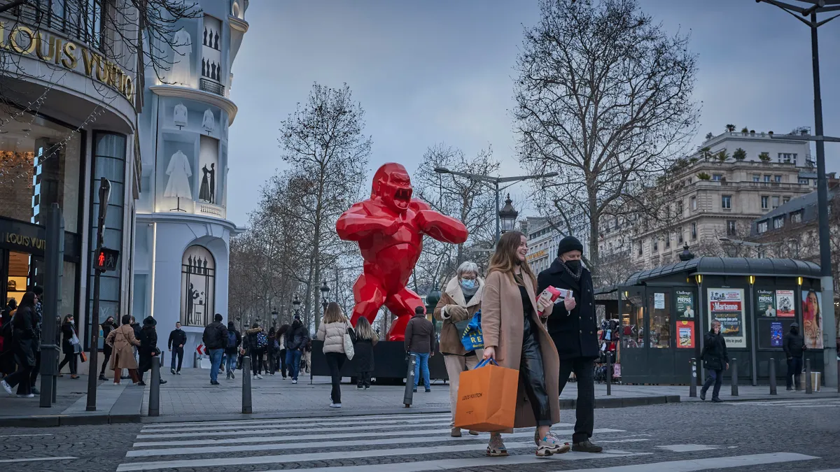 Three people walk across a crosswalk in front of Louis Vuitton store.