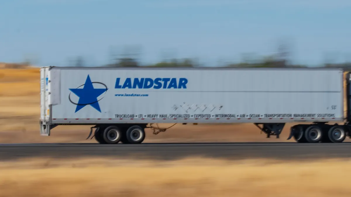 A Landstar System trailer on an interstate with blue sky and a blurred landscape in the background.