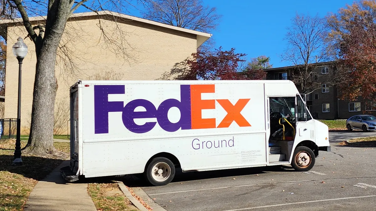 A white delivery truck with the red and blue FedEx logo parked at a apartment complex.