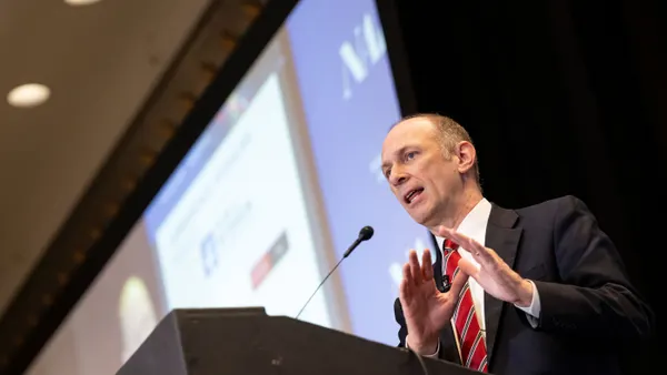 Chicago Federal Reserve President Austan Goolsbee stands at podium with hands up and lighted screen behind.