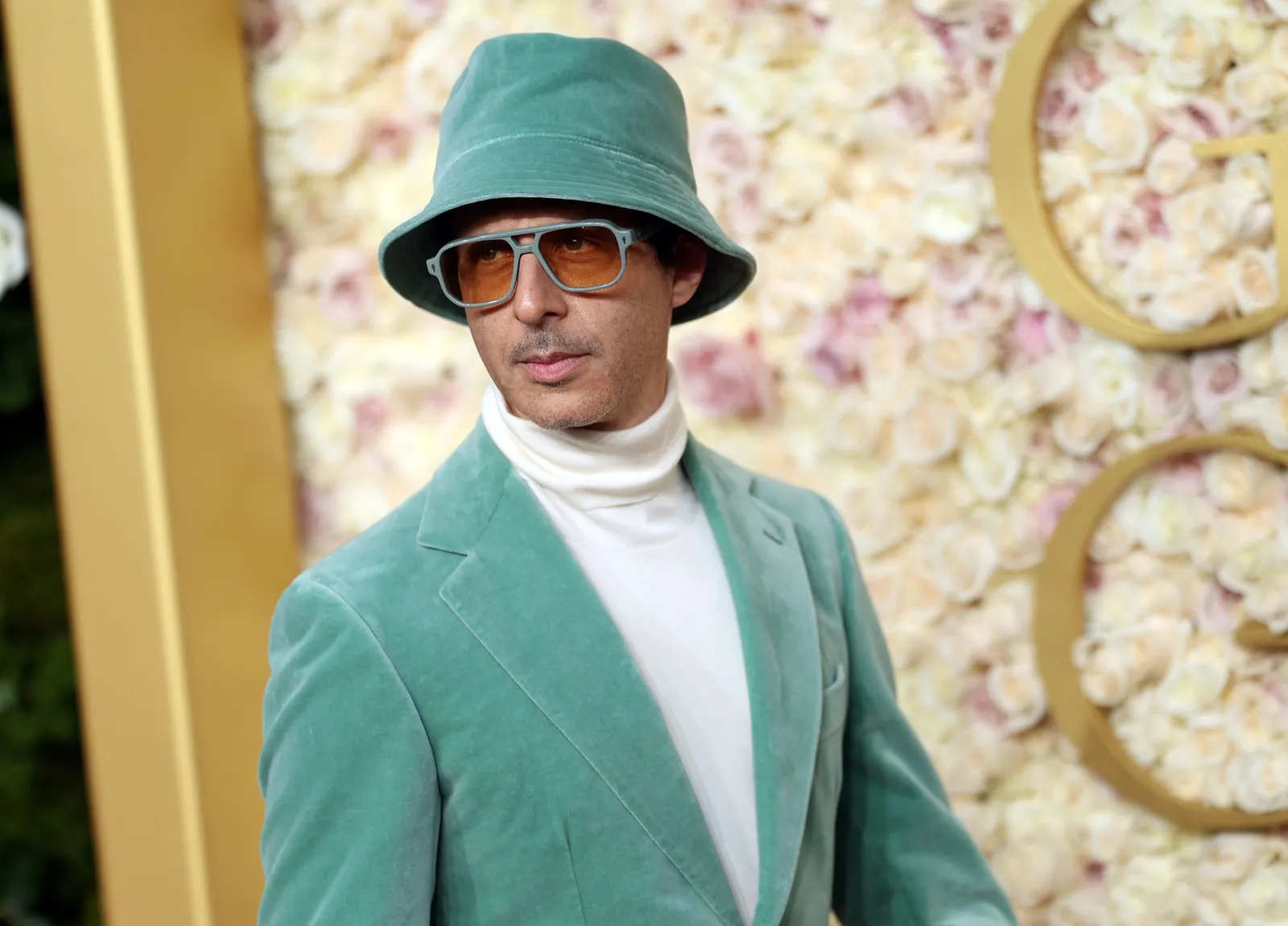 A person in a white turtleneck, a mint green suit, bucket hat and sunglasses.