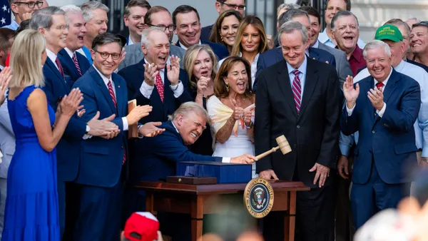 A crowd of people surround President Donald Trump outside as he raises a gavel at a podium in a celebratory fashion.