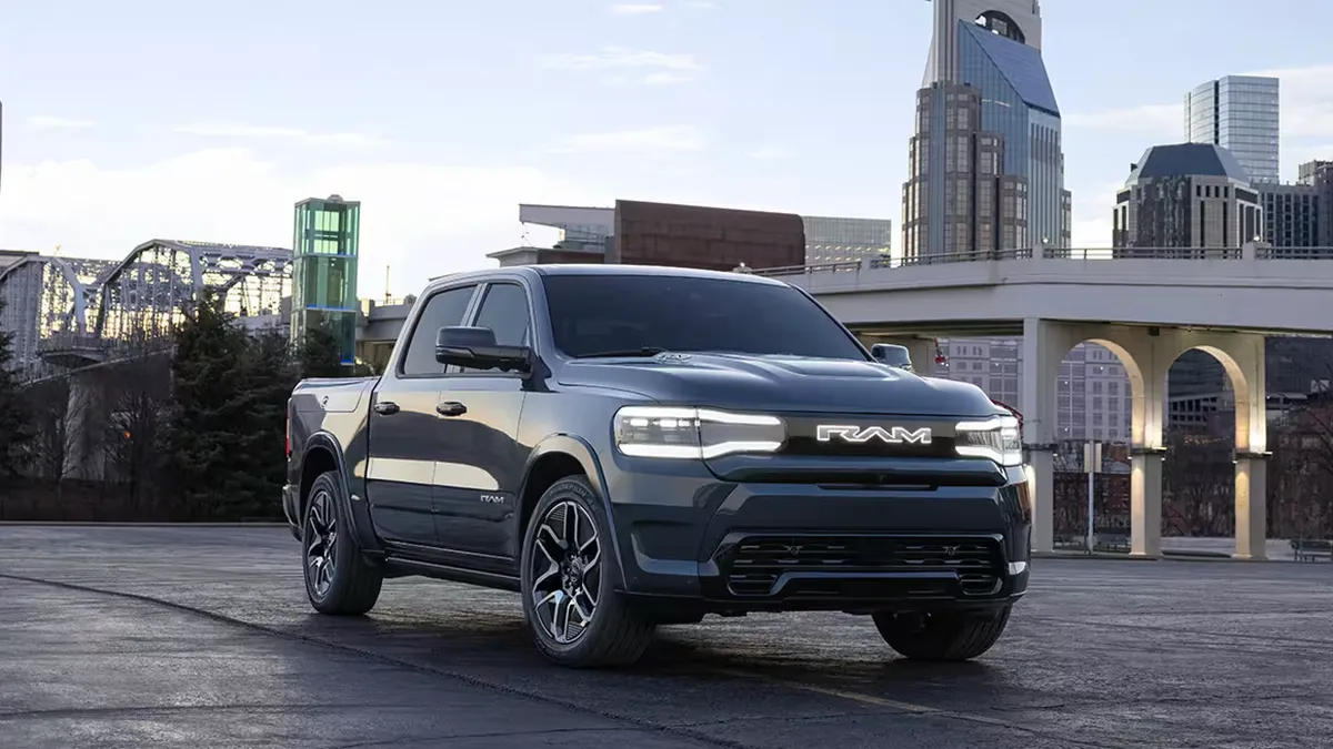 The Ram 1500 REV pickup parked in an urban area with a bridge and building in the background.