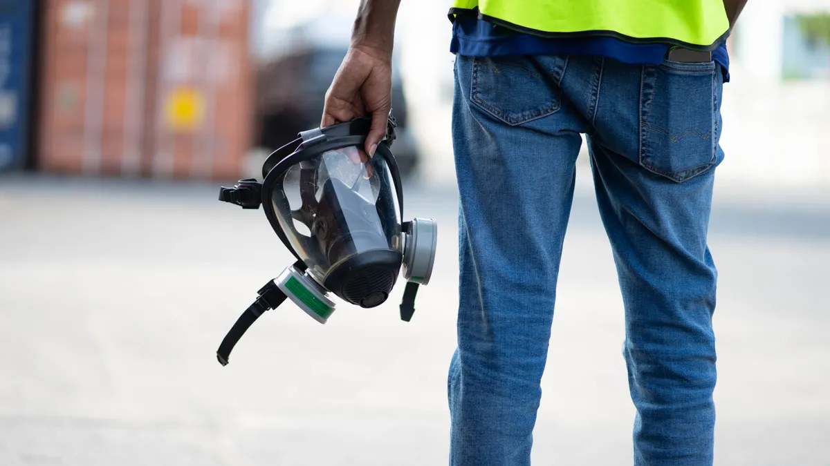 A waist-down photo of a man in jeans holding a respirator.