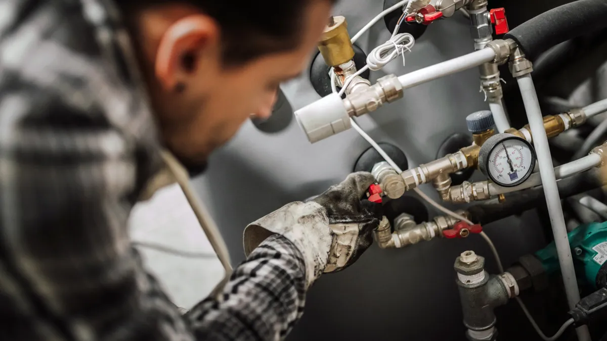 Close-up of a gloved worker fixing pipes on a heating system.