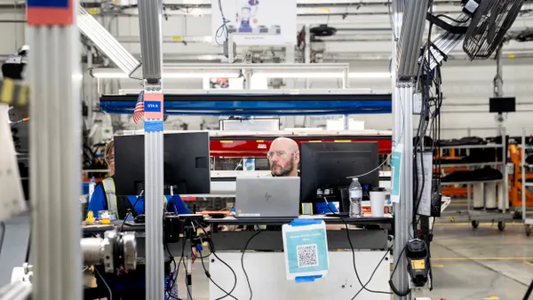 Two employees check computer monitors inside a plant.
