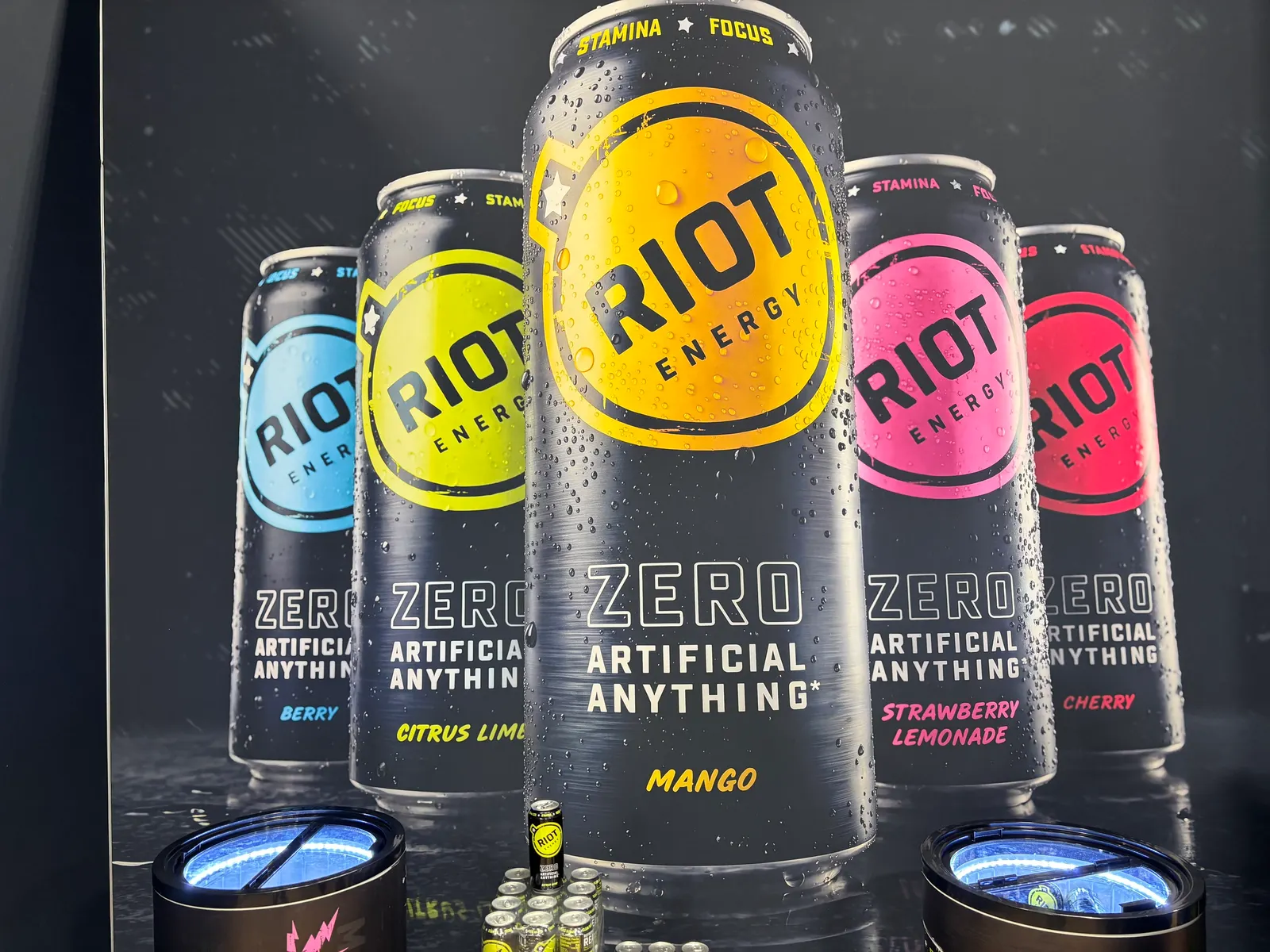 A photo of an advertisement showing cans of energy drinks against a black background. The cans say Riot Energy. Zero artificial anything. "