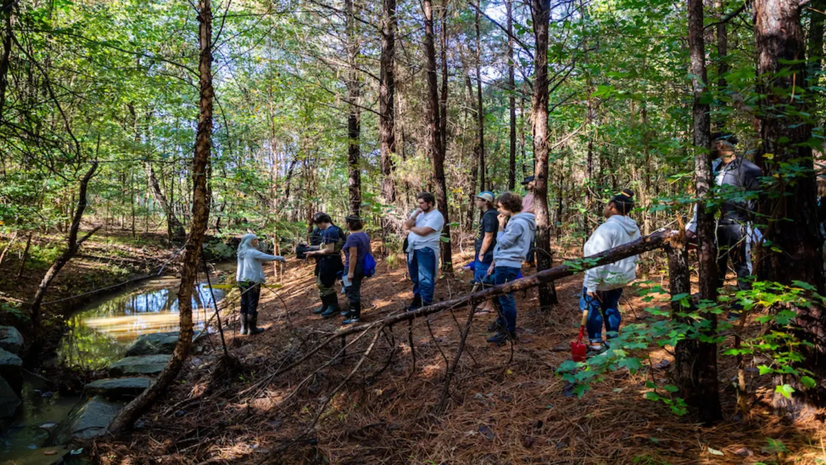 Students standing in woods near a creek facing instructor.